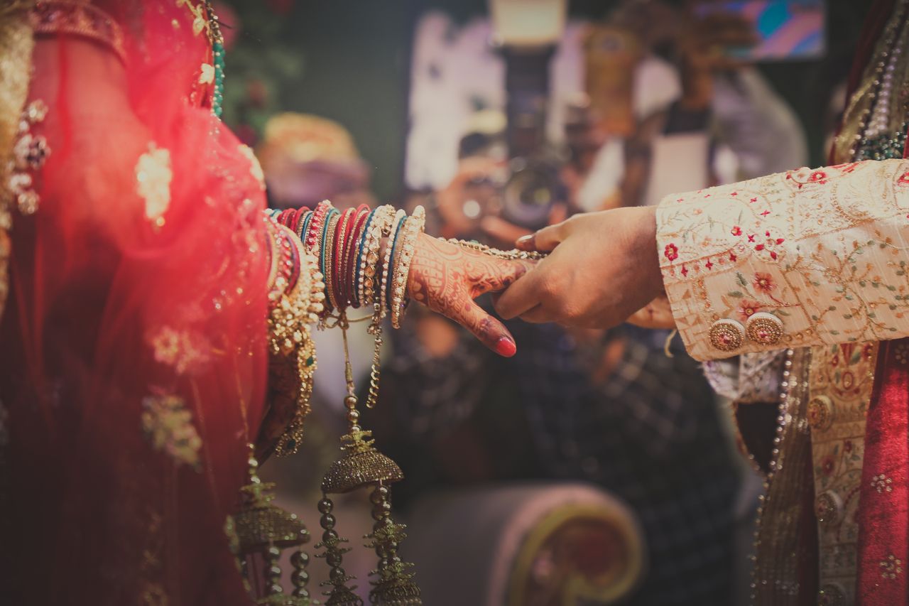 Close-up of a bride and groom's hands adorned with henna and jewelry during a traditional Indian wedding ceremony.