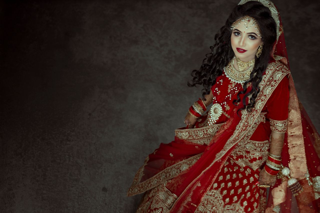 contact-img Stunning portrait of a bride in red traditional attire adorned with jewelry, showcasing intricate henna designs.