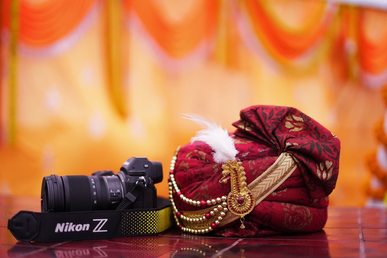 gallery-3 Vibrant Indian turban with adornments beside a professional camera, perfect for cultural and photography themes.