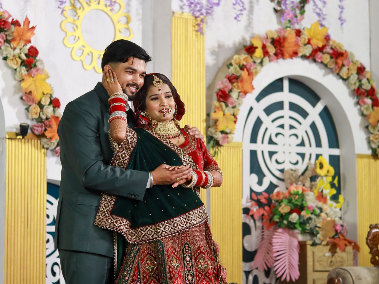 gallery-5 Beautiful Indian couple in traditional wedding attire, embracing at a vibrant indoor ceremony.