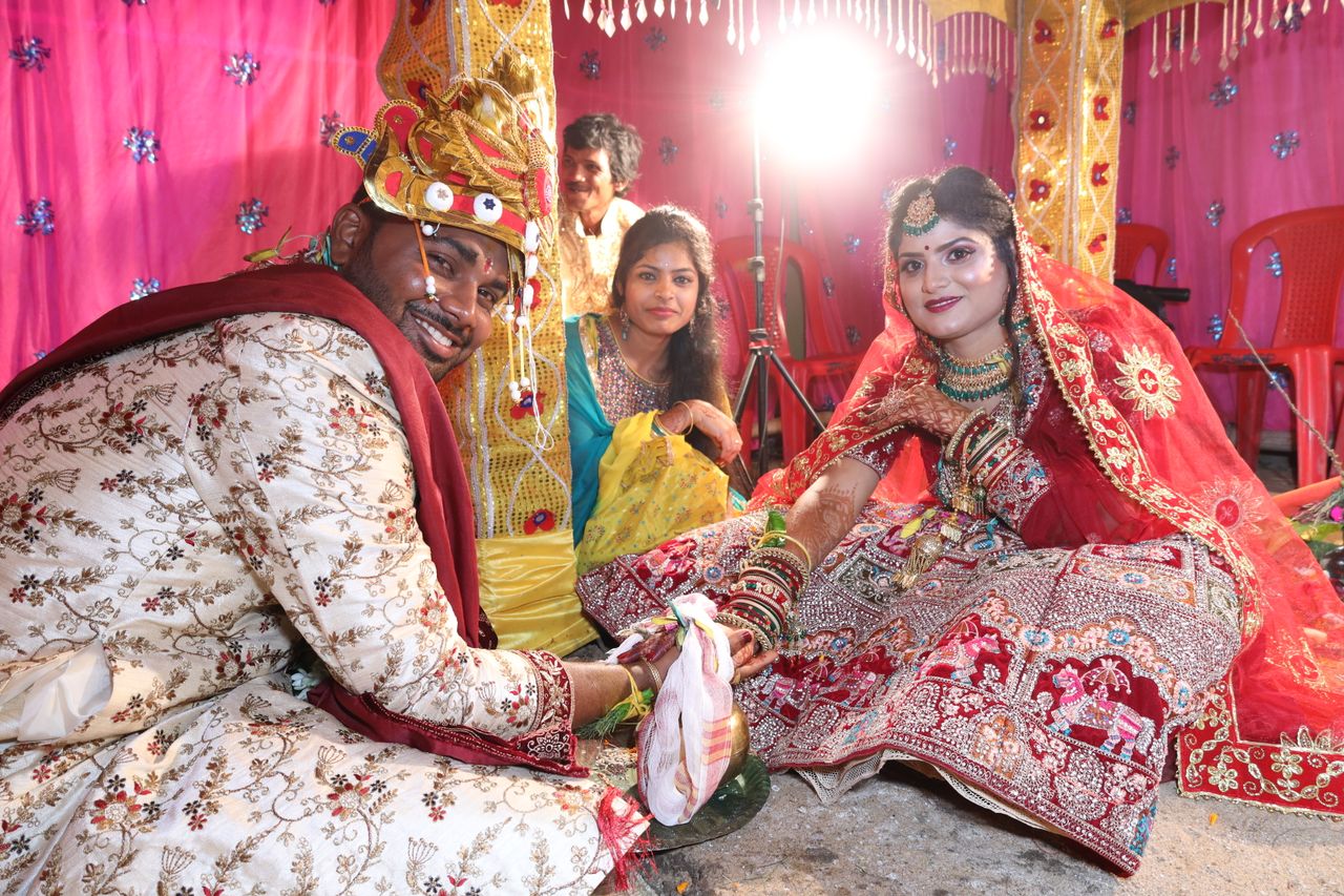 Joyful Indian wedding scene capturing bride and groom in elegant traditional attire, smiling and holding hands.