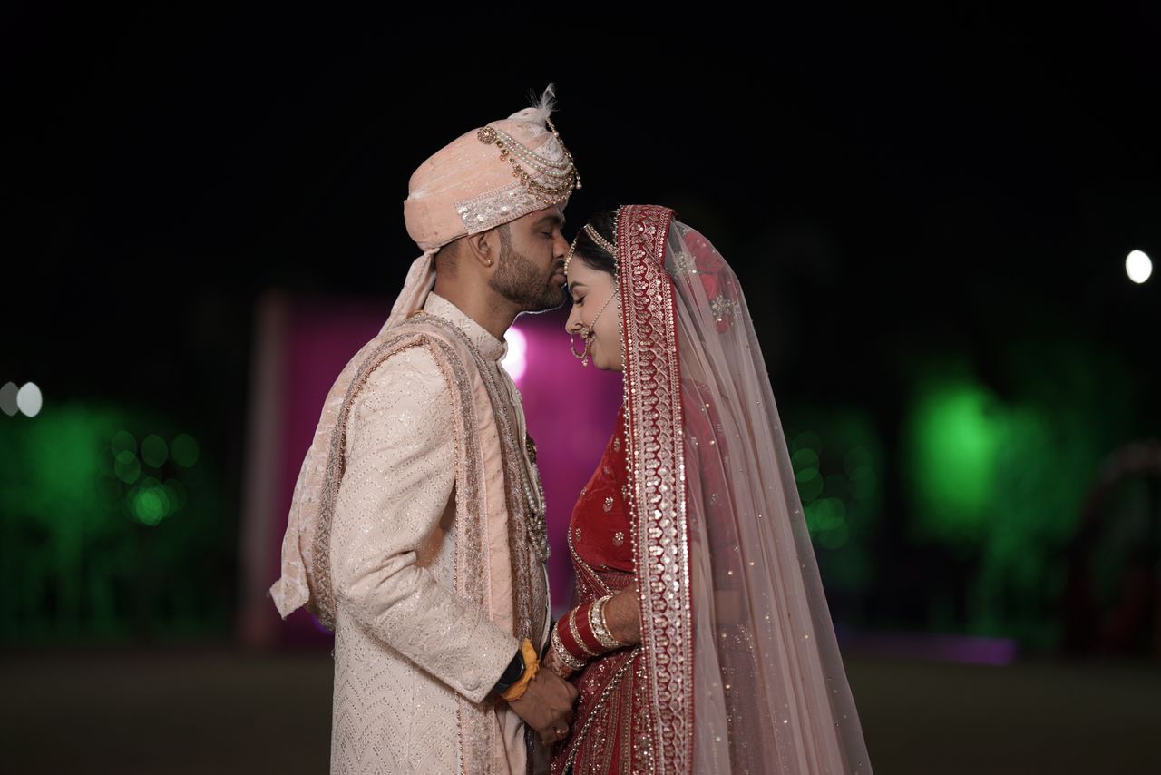 about-02 A joyful Indian couple in traditional attire shares an intimate moment during a night wedding ceremony.