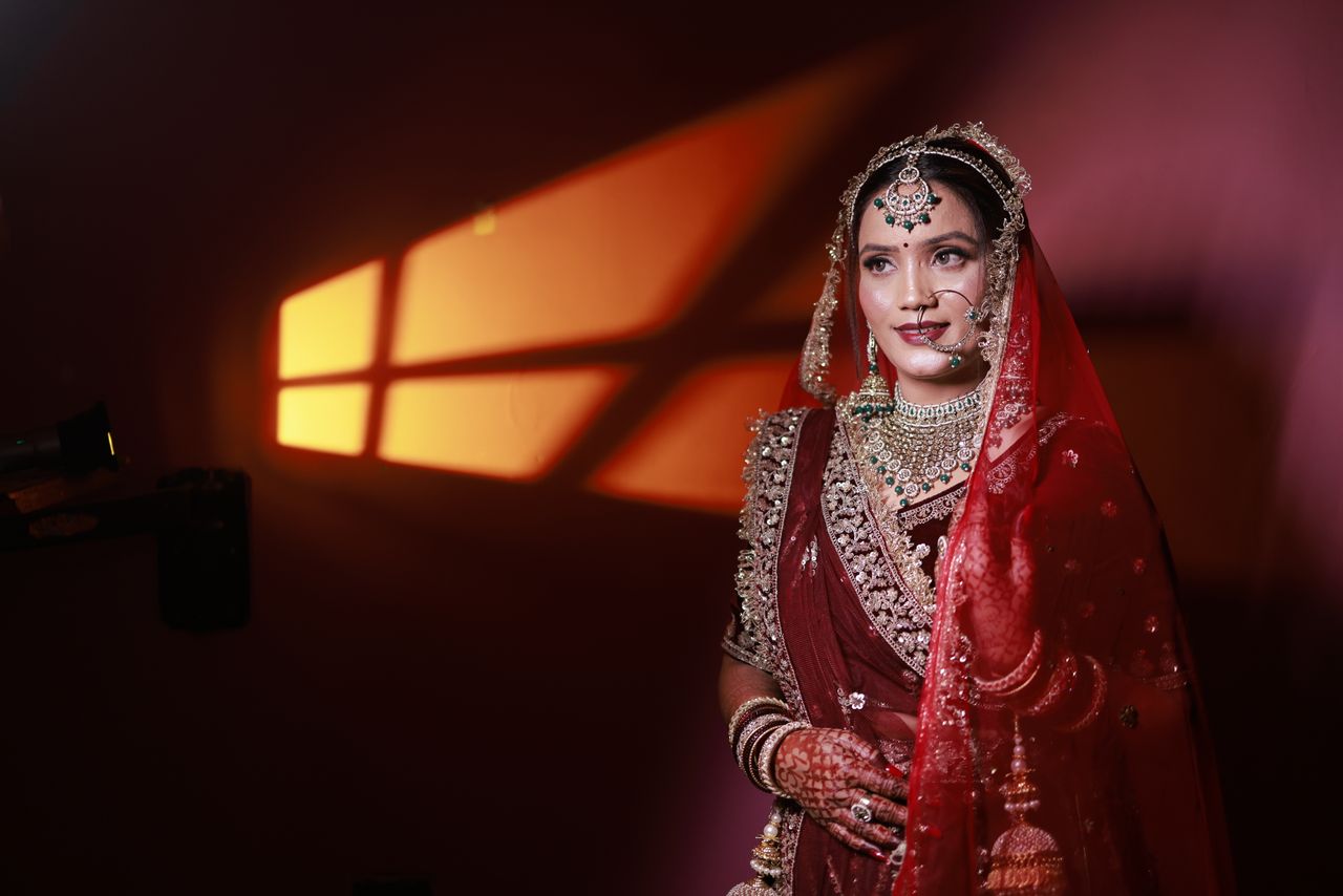 hero-img-02 Stunning Indian bride in red saree with intricate jewelry under warm light.