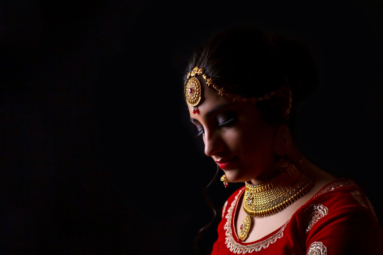 gallery-1 Portrait of an Indian woman adorned with golden jewelry on a dark background.